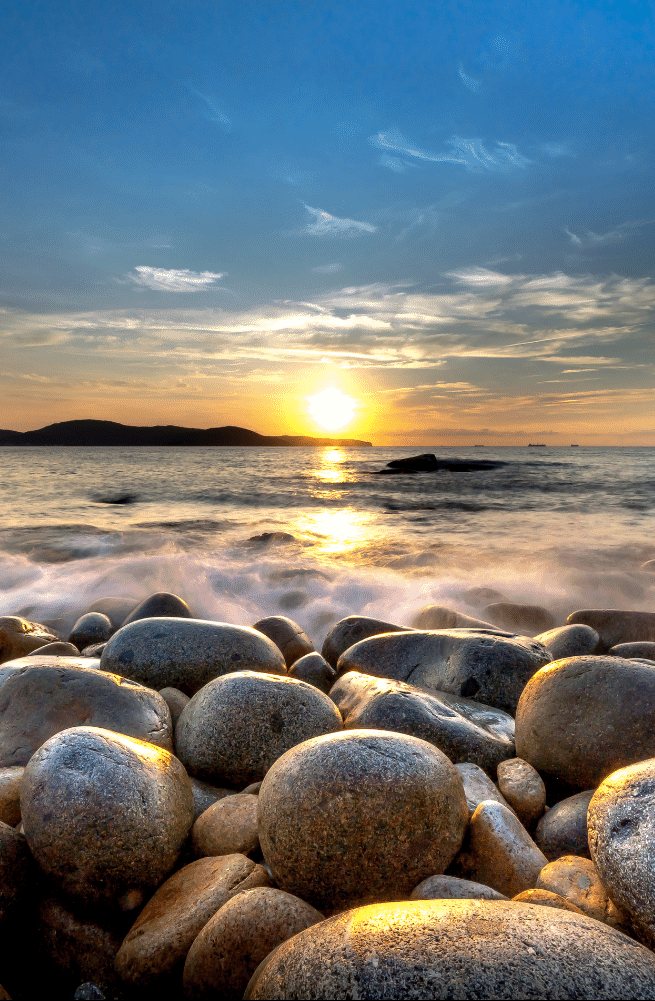 Boulders at the shoreline, sun on the horizon